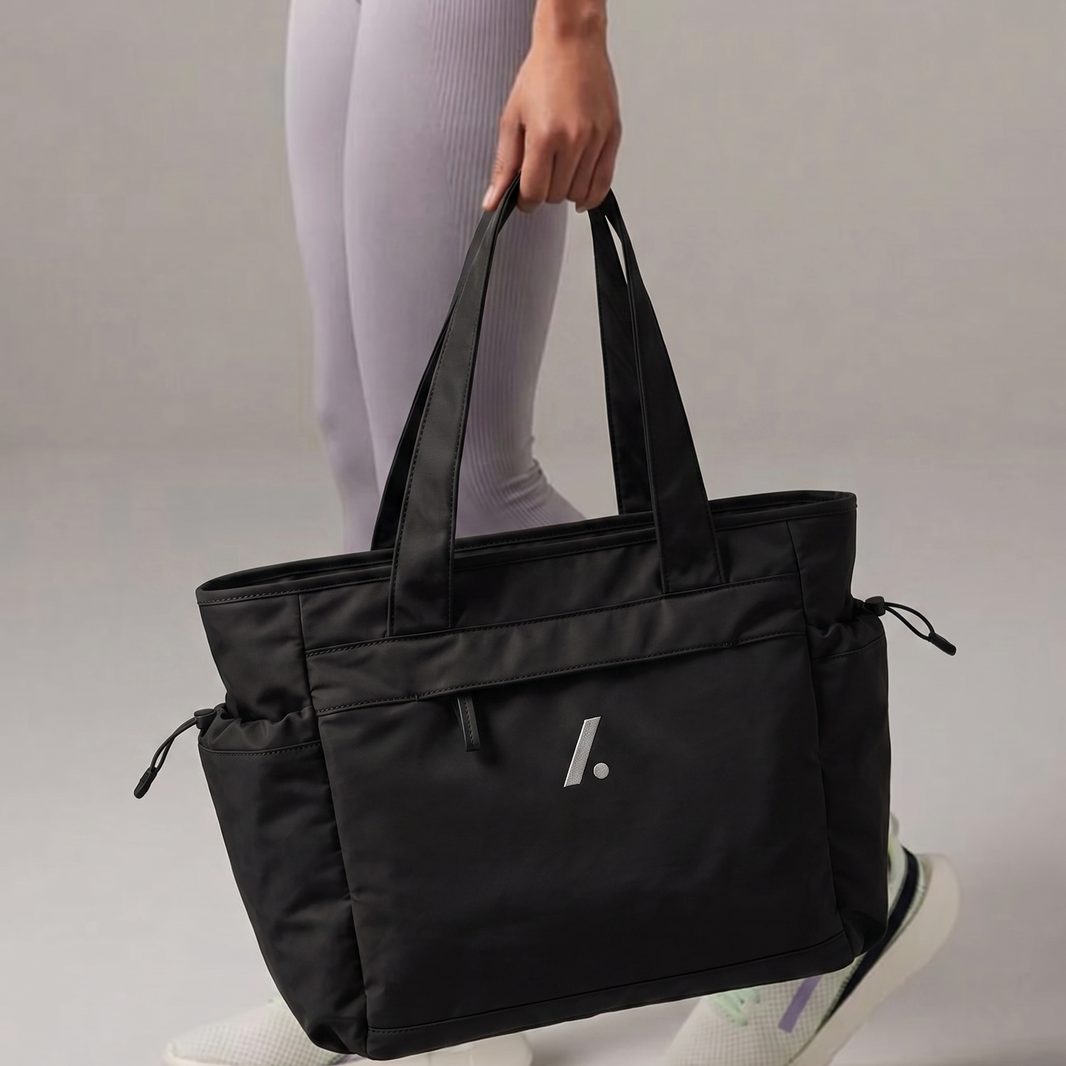 Person holding a black tote bag with a logo on a gray background