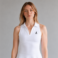 A woman wearing a white sleeveless collared tennis dress with a small black logo on the left chest, photographed against a neutral gray studio background.
