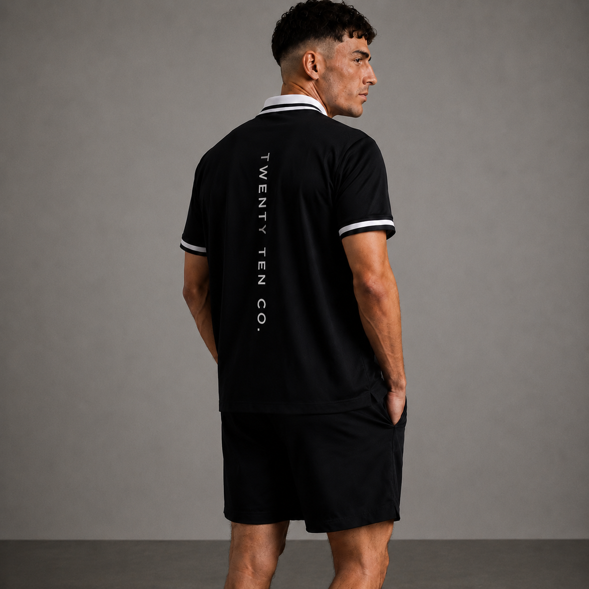 Man wearing a black polo shirt with 'TWENTY TEN CO.' branding on the back against a gray background