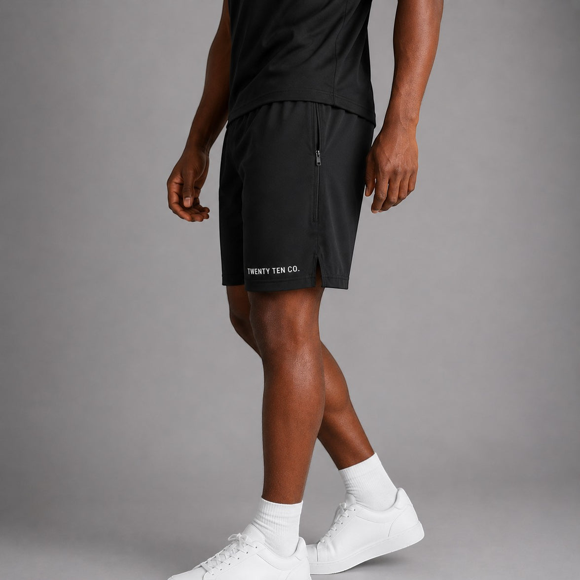 Twenty Ten Co. black athletic performance shorts with zippered pockets and elastic waistband. Model is wearing white socks and sneakers.