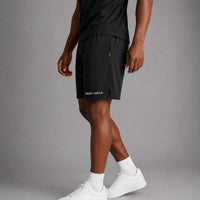 Twenty Ten Co. black athletic performance shorts with zippered pockets and elastic waistband. Model is wearing white socks and sneakers.