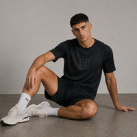 TwentyTenCollective black athletic t-shirt with raglan sleeves and tonal chest logo, worn by a man sitting on the floor.