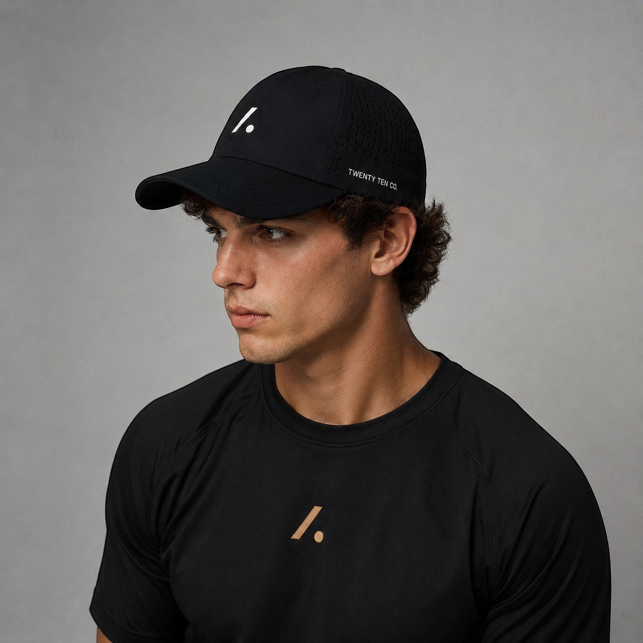 TwentyTenCo black performance baseball cap with white logo and perforated sides, worn by a man.