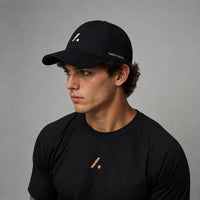 TwentyTenCo black performance baseball cap with white logo and perforated sides, worn by a man.