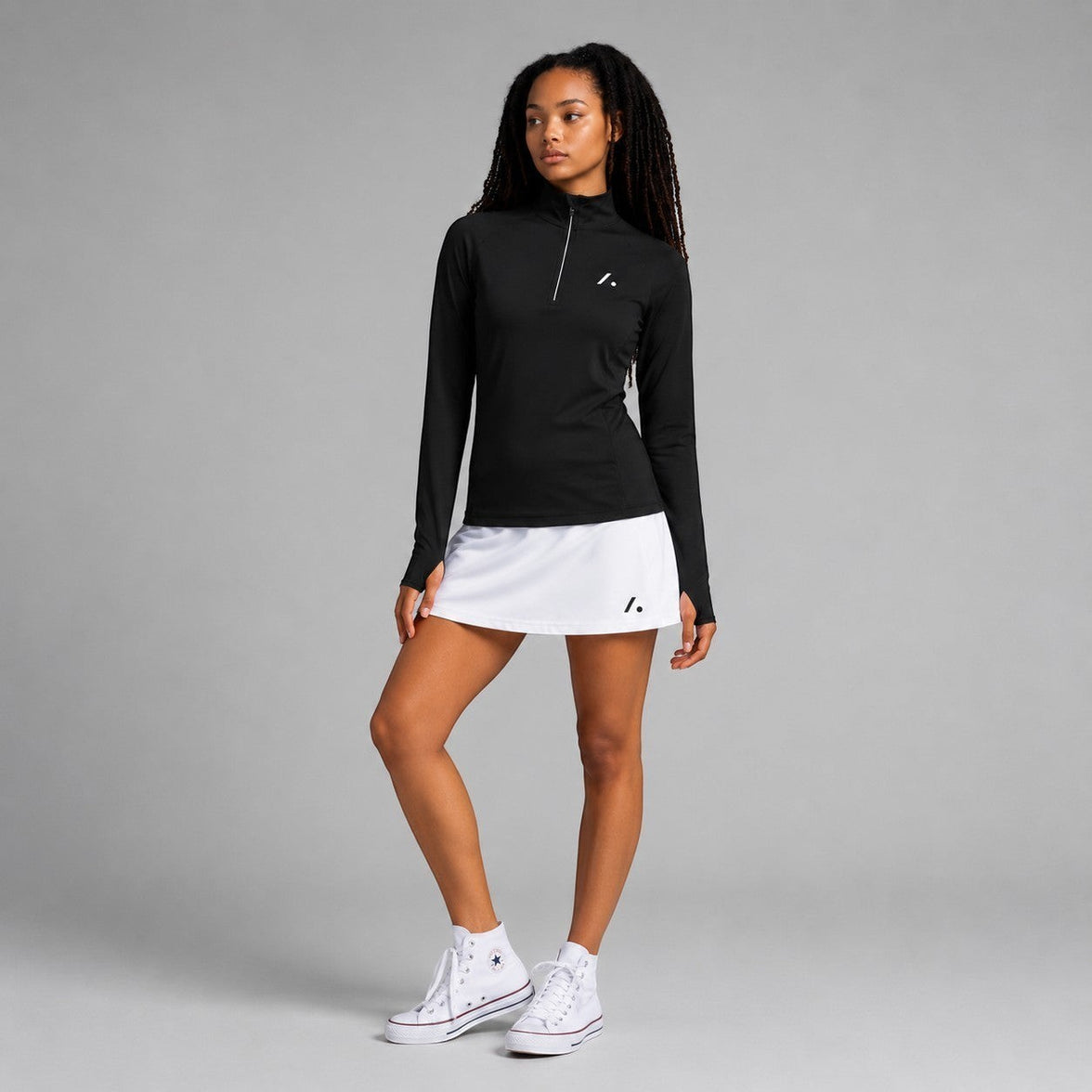 TwentyTenCollective black long sleeve quarter zip athletic top with thumbholes and white trim. Model wears with white skort.