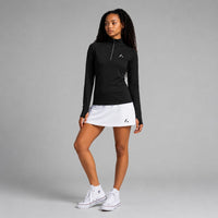 TwentyTenCollective black long sleeve quarter zip athletic top with thumbholes and white trim. Model wears with white skort.