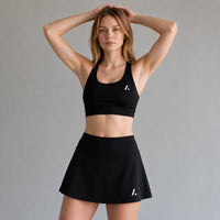 TwentyTenCollective black athletic sports bra and skort set with white logo detail. Model is wearing a size medium.