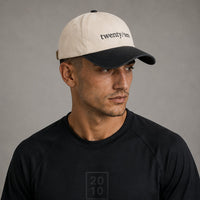 TwentyTenCollective two-tone baseball cap in cream and charcoal grey cotton with embroidered logo and adjustable strap.
