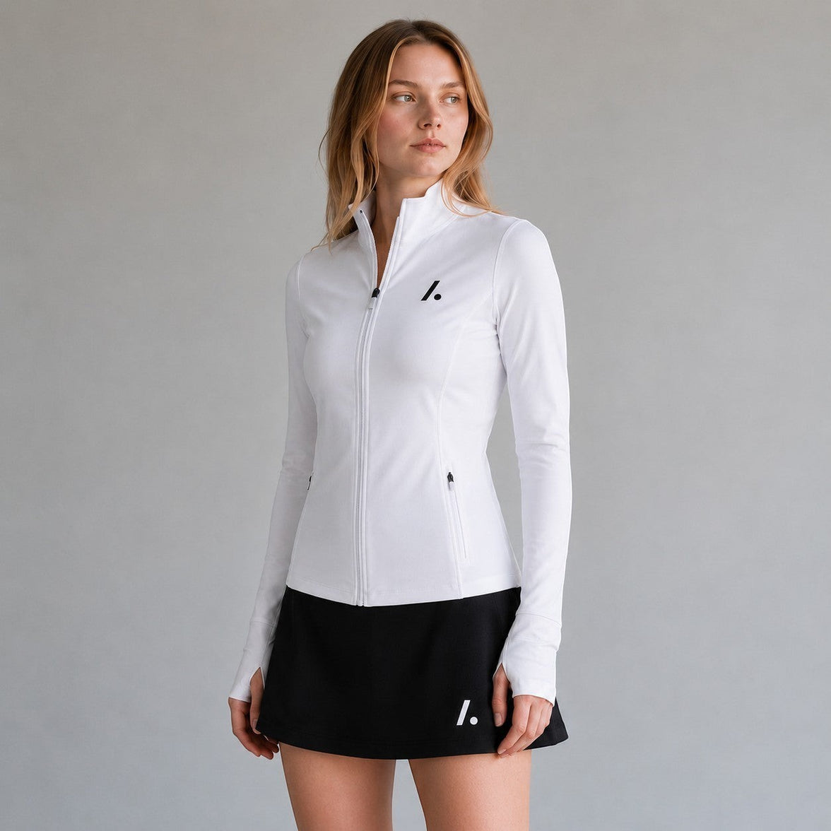 TwentyTenCollective white athletic full-zip jacket with mock neck, thumbholes, and zippered pockets. Model is wearing a black skirt.