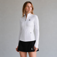 TwentyTenCollective white athletic full-zip jacket with mock neck, thumbholes, and zippered pockets. Model is wearing a black skirt.
