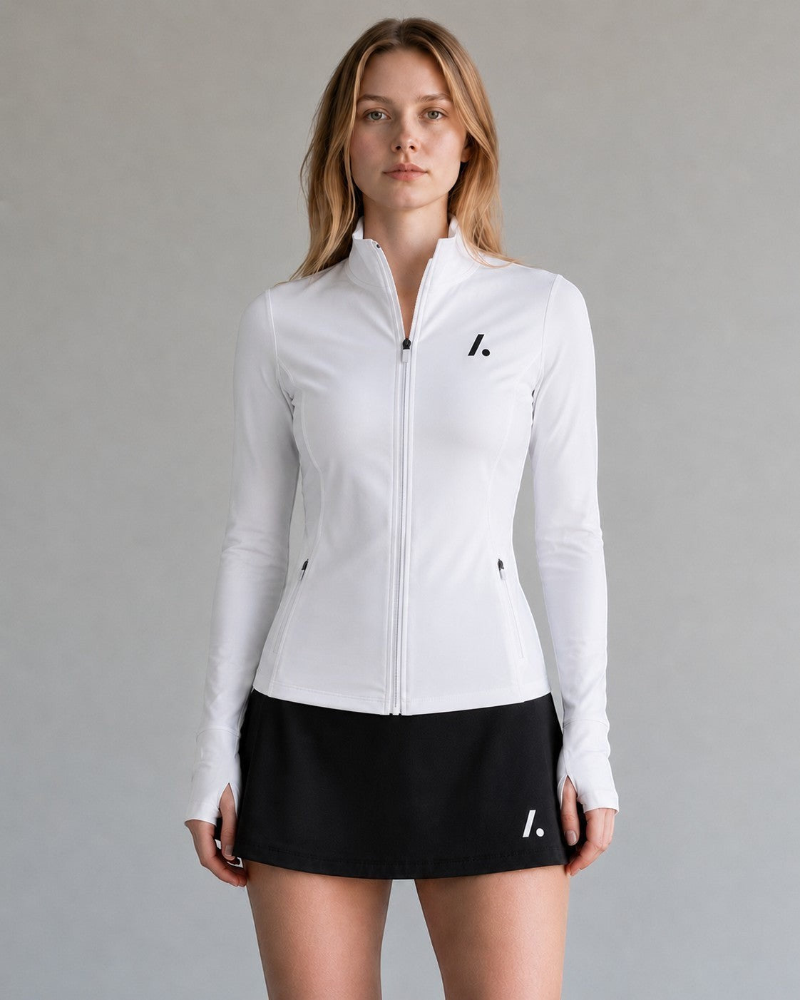 TwentyTenCollective white athletic full zip jacket with mock neck, thumbholes, and zippered pockets. Model wears a black skirt.