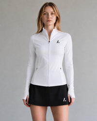 TwentyTenCollective white athletic full zip jacket with mock neck, thumbholes, and zippered pockets. Model wears a black skirt.