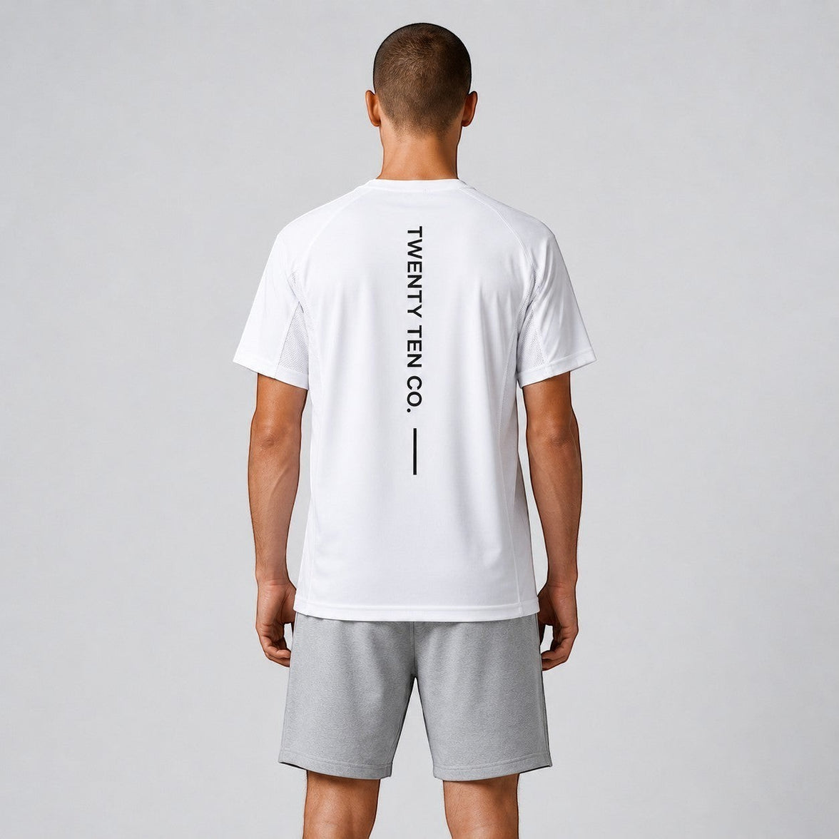 TwentyTenCollective white athletic performance t-shirt with vertical logo detail and grey shorts. Model from behind.