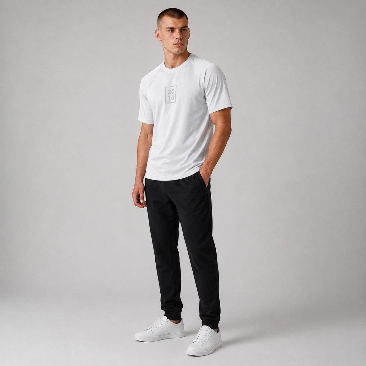 TwentyTenCollective white performance athletic t-shirt with crew neck and subtle chest graphic. Model is wearing black pants and white sneakers.
