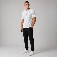TwentyTenCollective white performance athletic t-shirt with crew neck and subtle chest graphic. Model is wearing black pants and white sneakers.