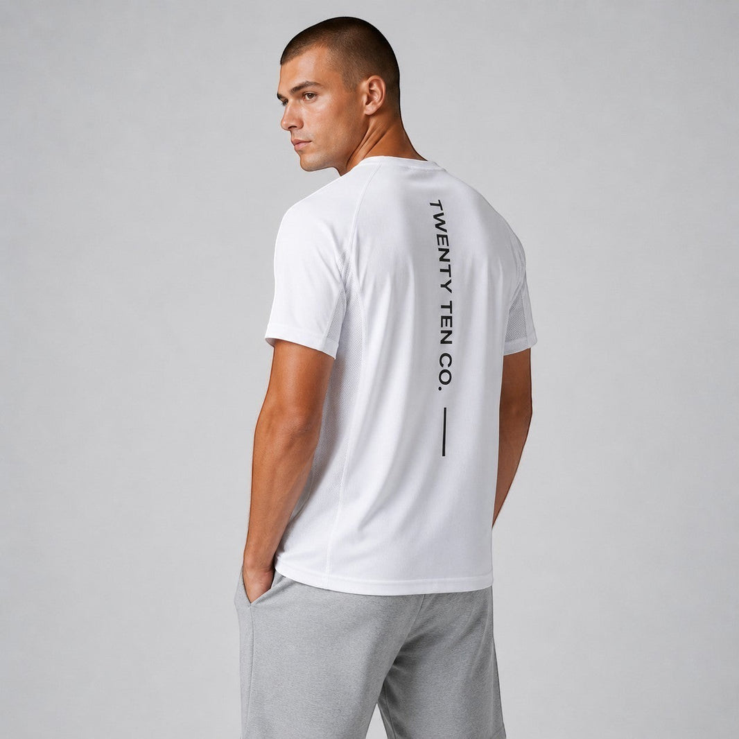 TwentyTenCollective white crew neck performance t-shirt with black vertical logo on back. Model wears grey shorts.