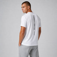 TwentyTenCollective white crew neck performance t-shirt with black vertical logo on back. Model wears grey shorts.