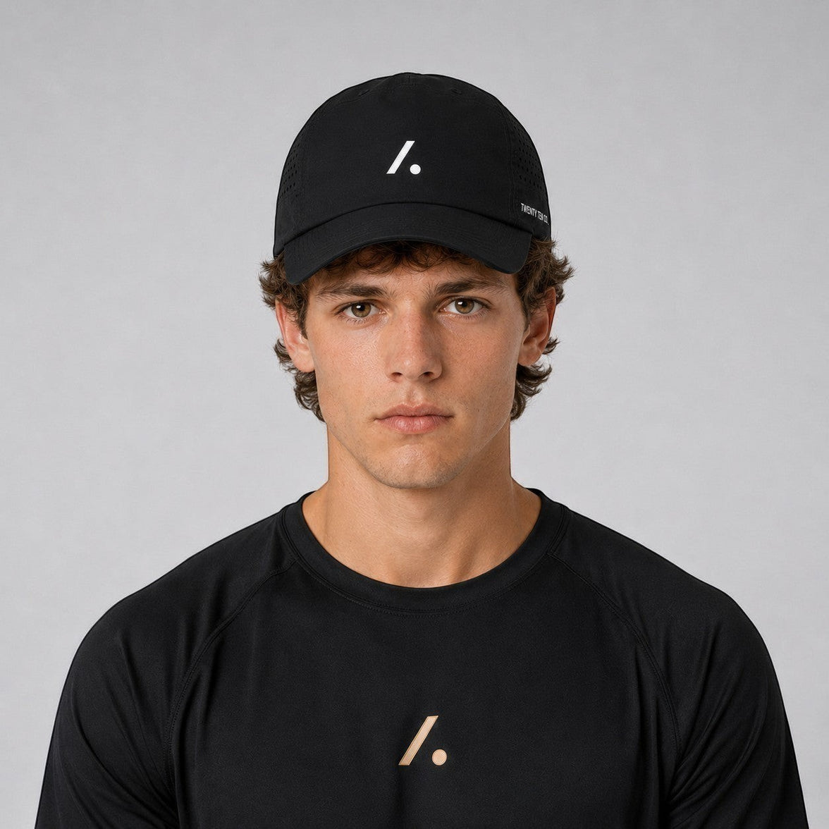 TwentyTenCo black performance baseball cap with white logo and perforated sides, worn by a man.