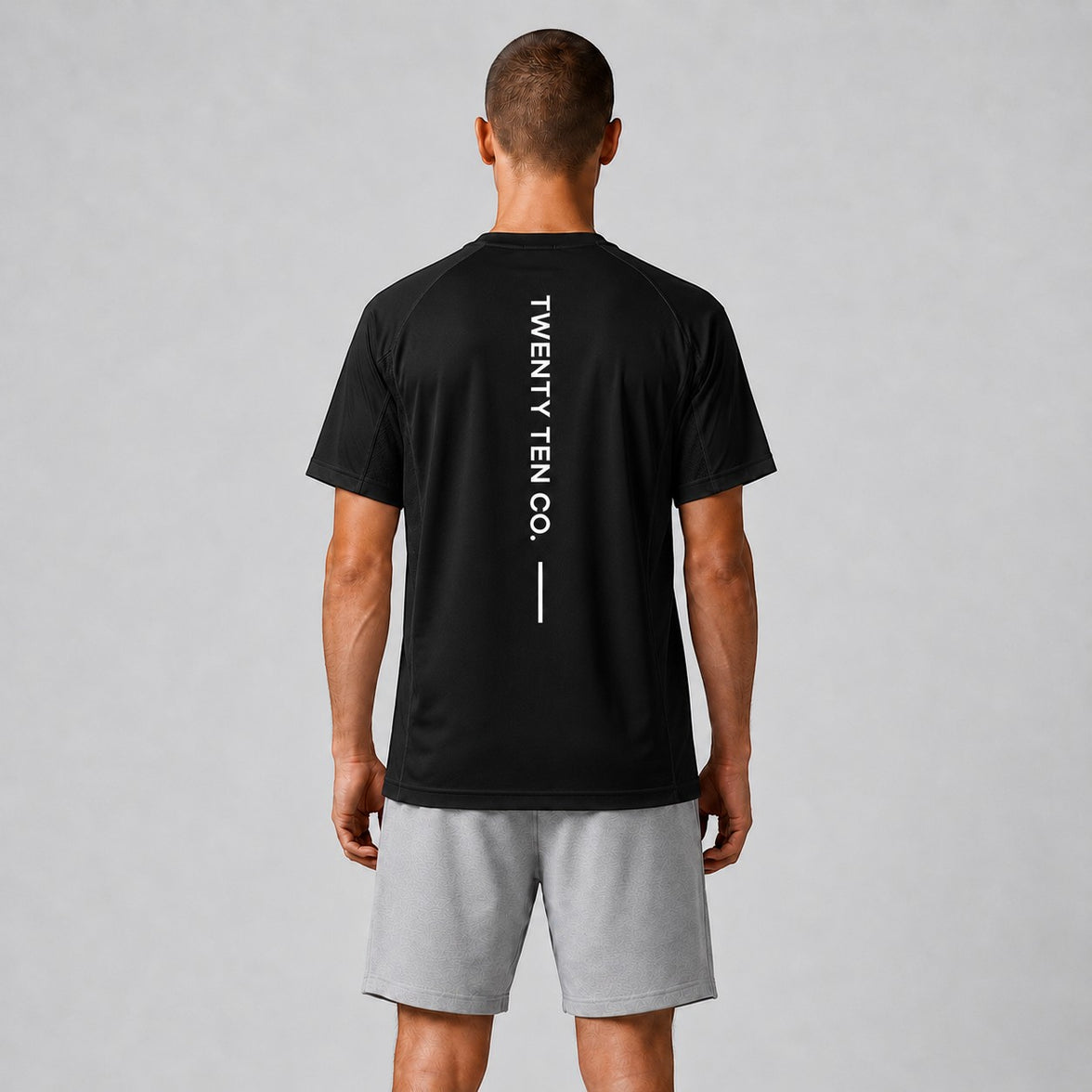 TwentyTenCo. black athletic t-shirt with vertical white TWENTY TEN CO. graphic on back. Model wears grey shorts.