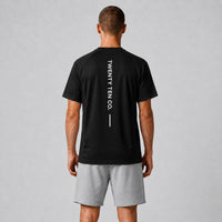 TwentyTenCo. black athletic t-shirt with vertical white TWENTY TEN CO. graphic on back. Model wears grey shorts.